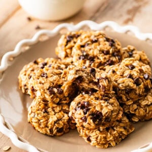 white platter with banana oatmeal cookies stacked in it. Glass of milk in the background.