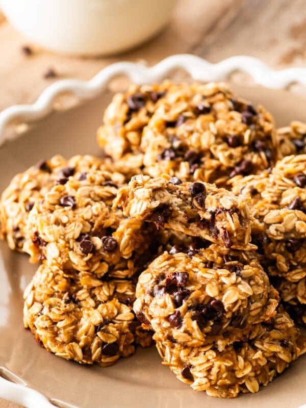 white platter with banana oatmeal cookies stacked in it. Glass of milk in the background.