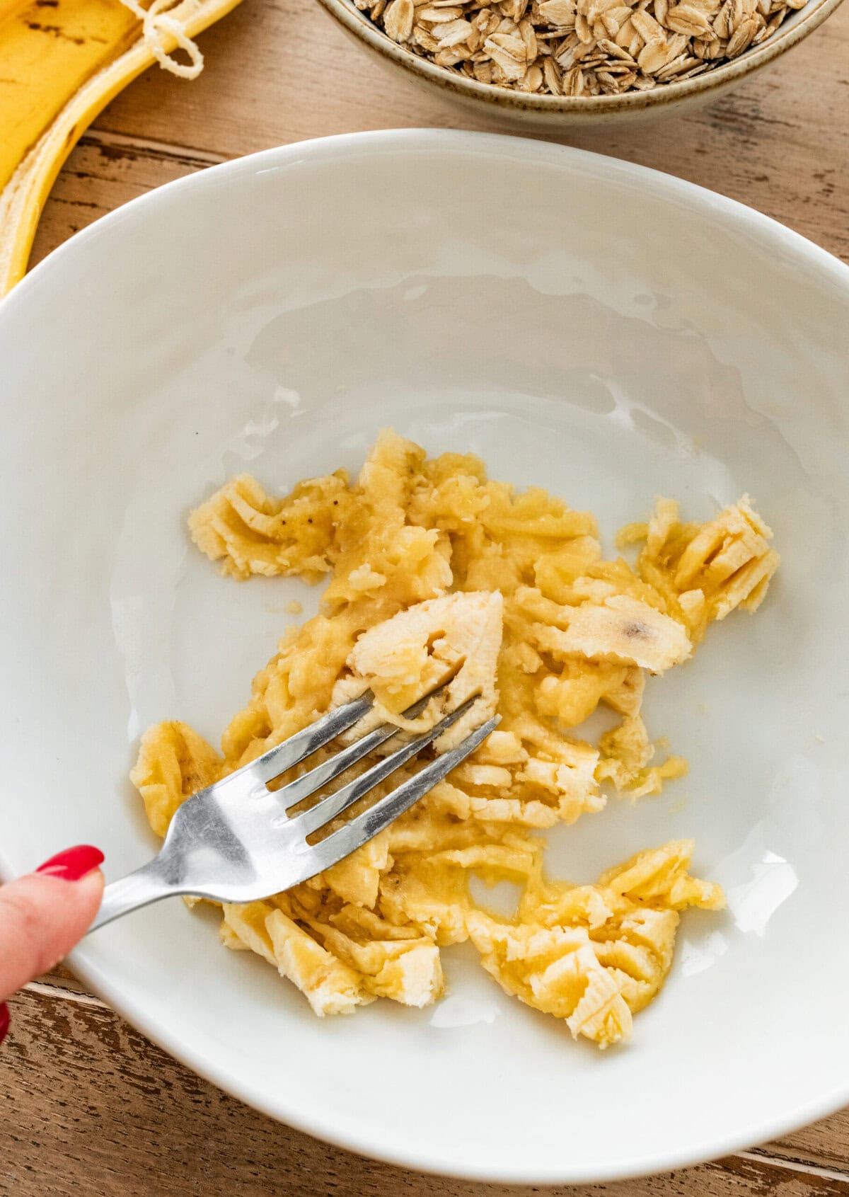 fork mashing banana in a white bowl.