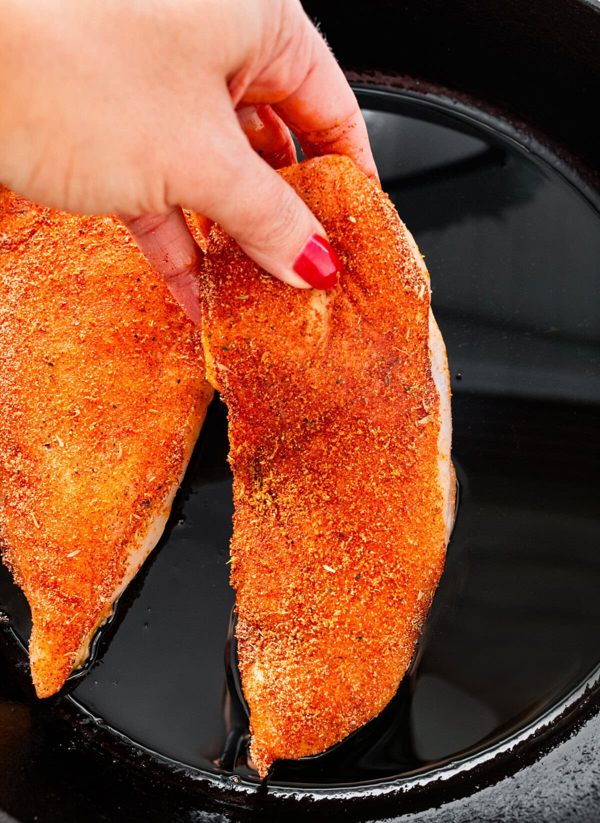 hand placing seasoned blackened chicken breasts on a hot cast iron pan.