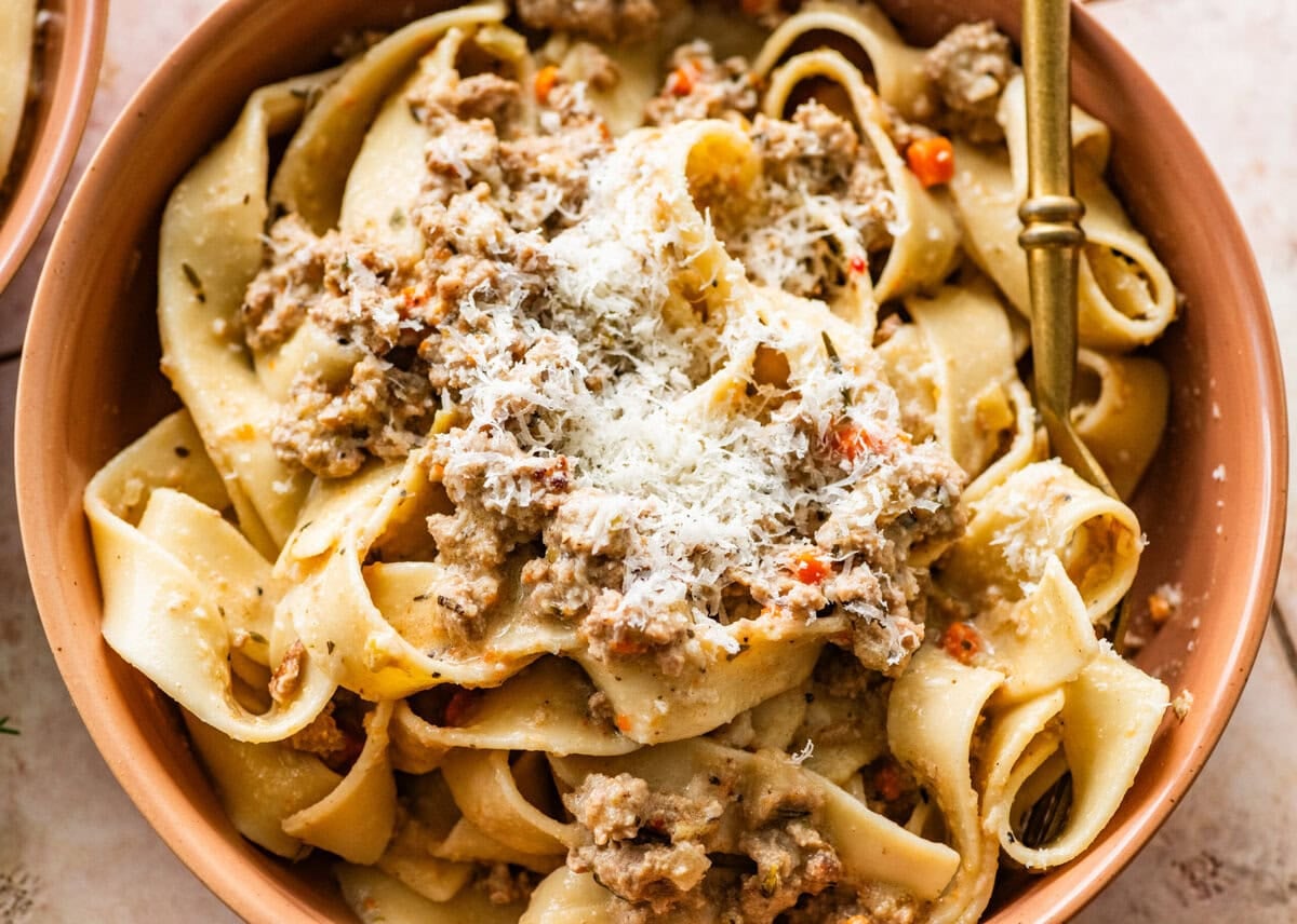 big bowl of white bolognese sauce with pappardelle pasta and parmesan cheese on top.