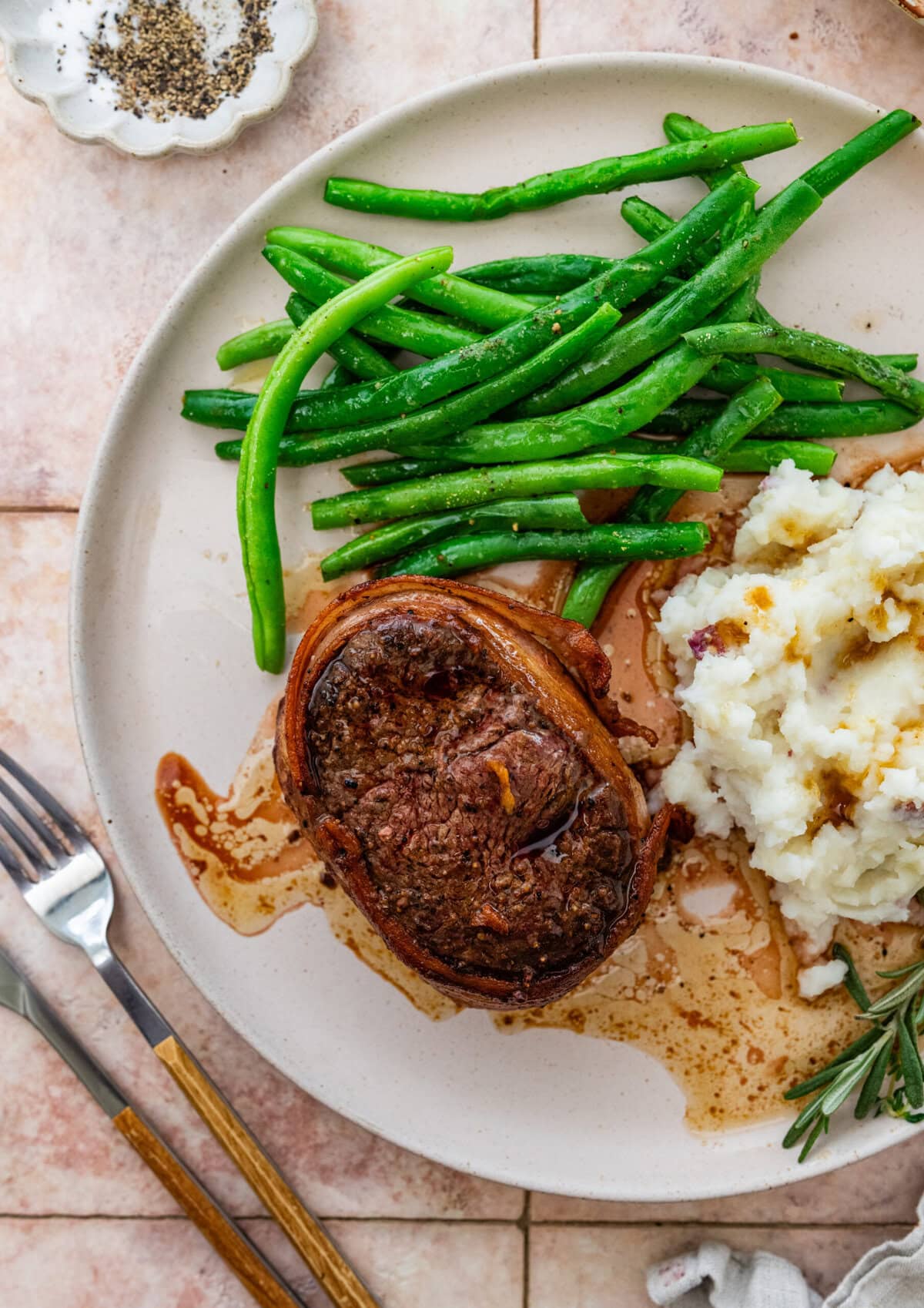 bacon wrapped filet mignon plated with potatoes and beans in the background.
