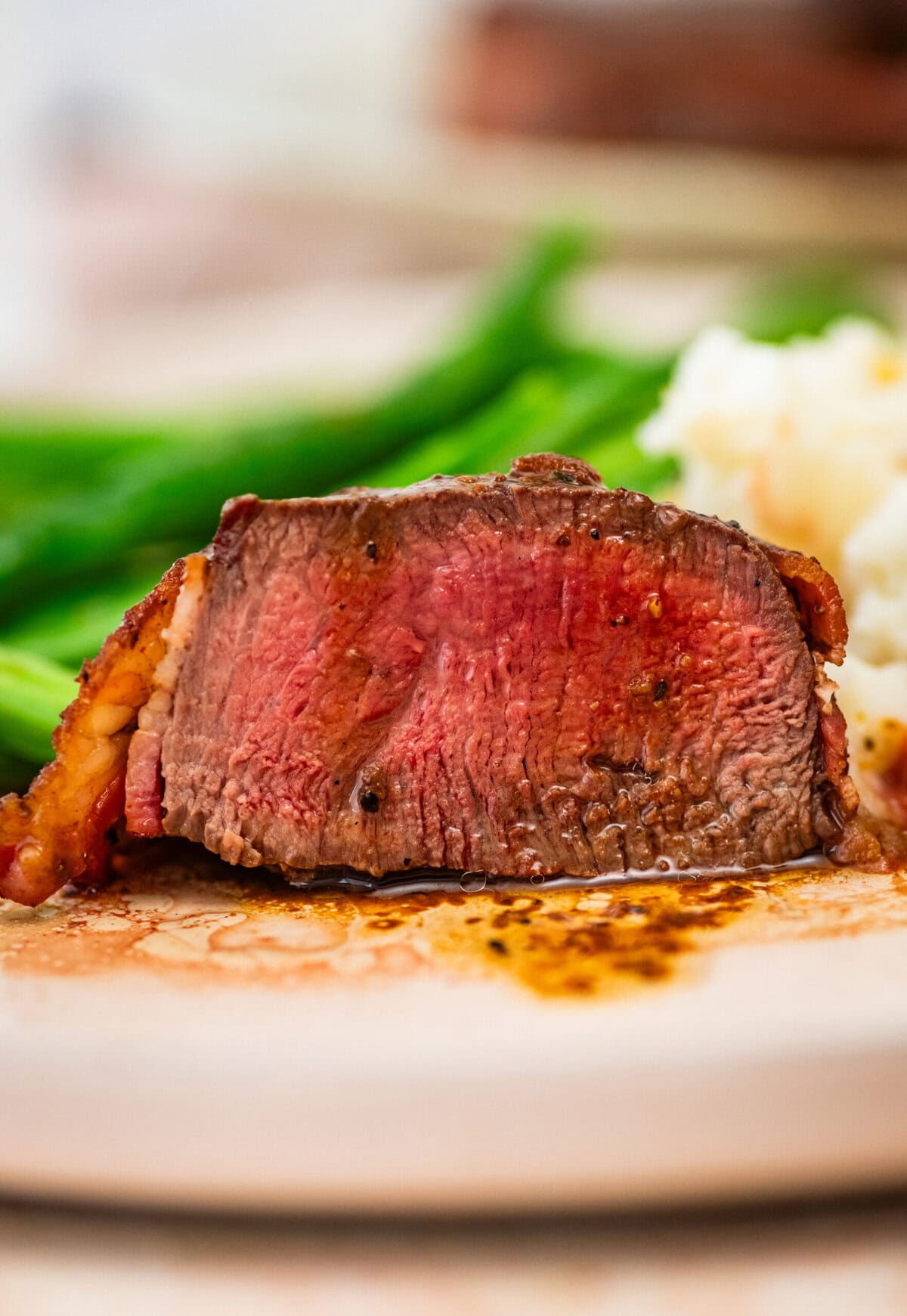 bacon wrapped filet mignon plated and sliced to show the perfect red center with potatoes and beans in the background.