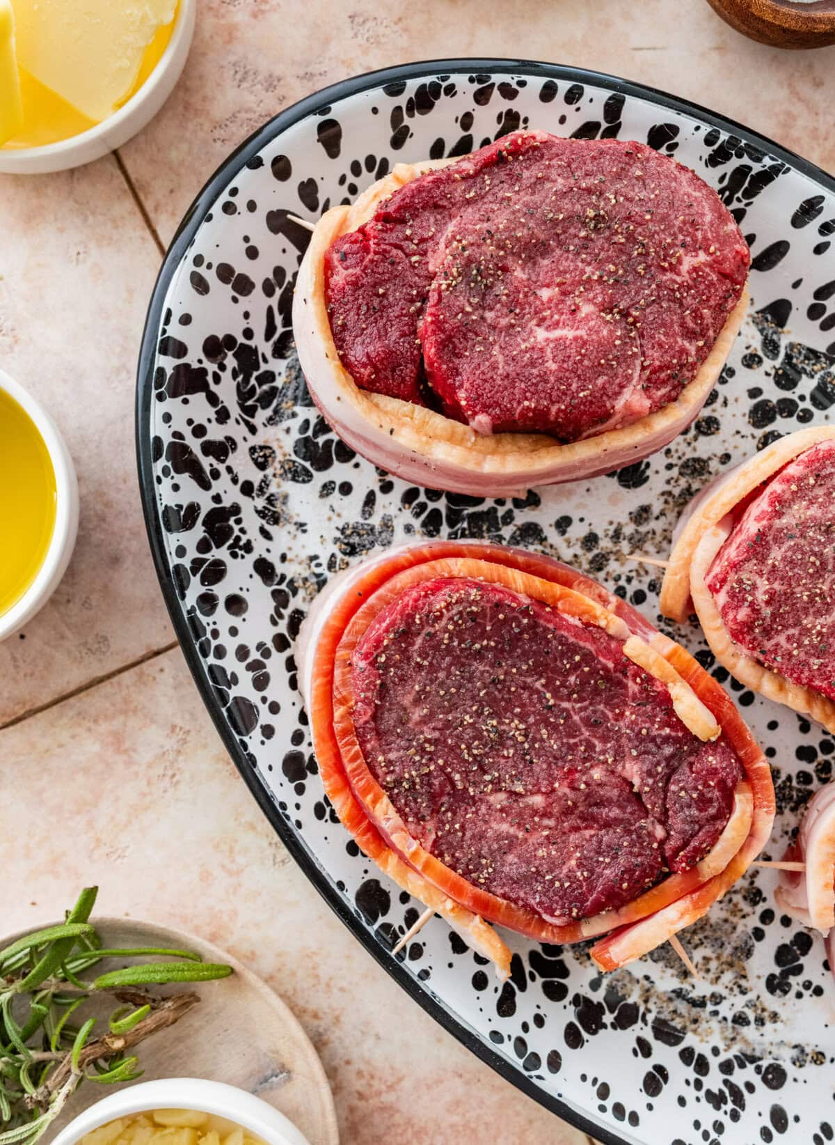 uncooked filet mignon steaks on a plate after seasoning with salt and pepper and wrapping with bacon.