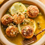 Chicken piccata meatballs in a bowl garnished with lemon and served with bread.