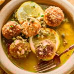 Chicken piccata meatballs in a bowl garnished with lemon.