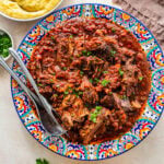 Italian pot roast with garnish on a serving plate with sides in the background.