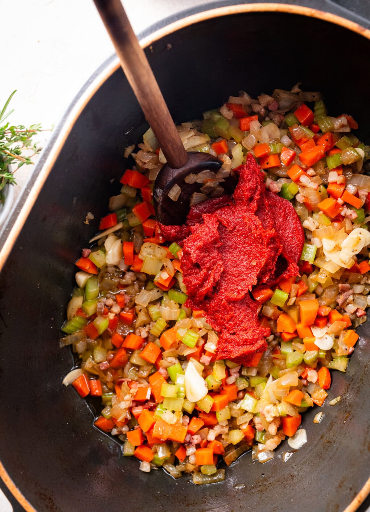 Tomato paste added to cooked vegetables in a pot with a wooden spoon mixing all ingredients together.