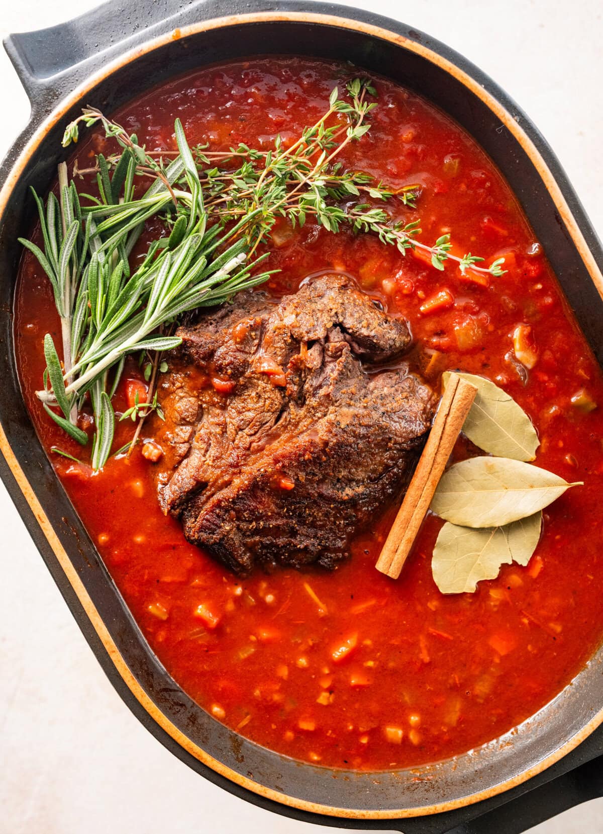 Cinnamon stick, bay leaves, and fresh herbs laying on top of the post roast.