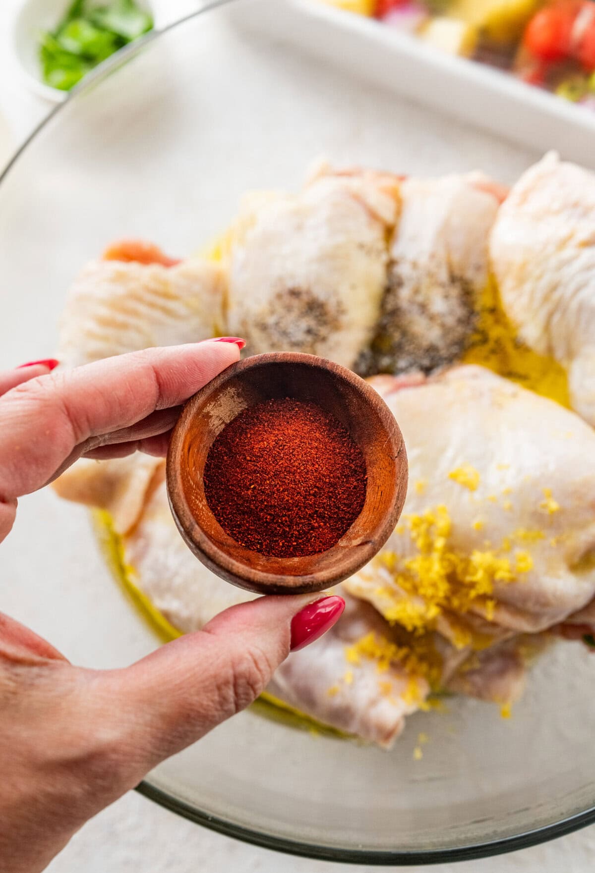 hand adding seasoning to chicken thighs in a large bowl.