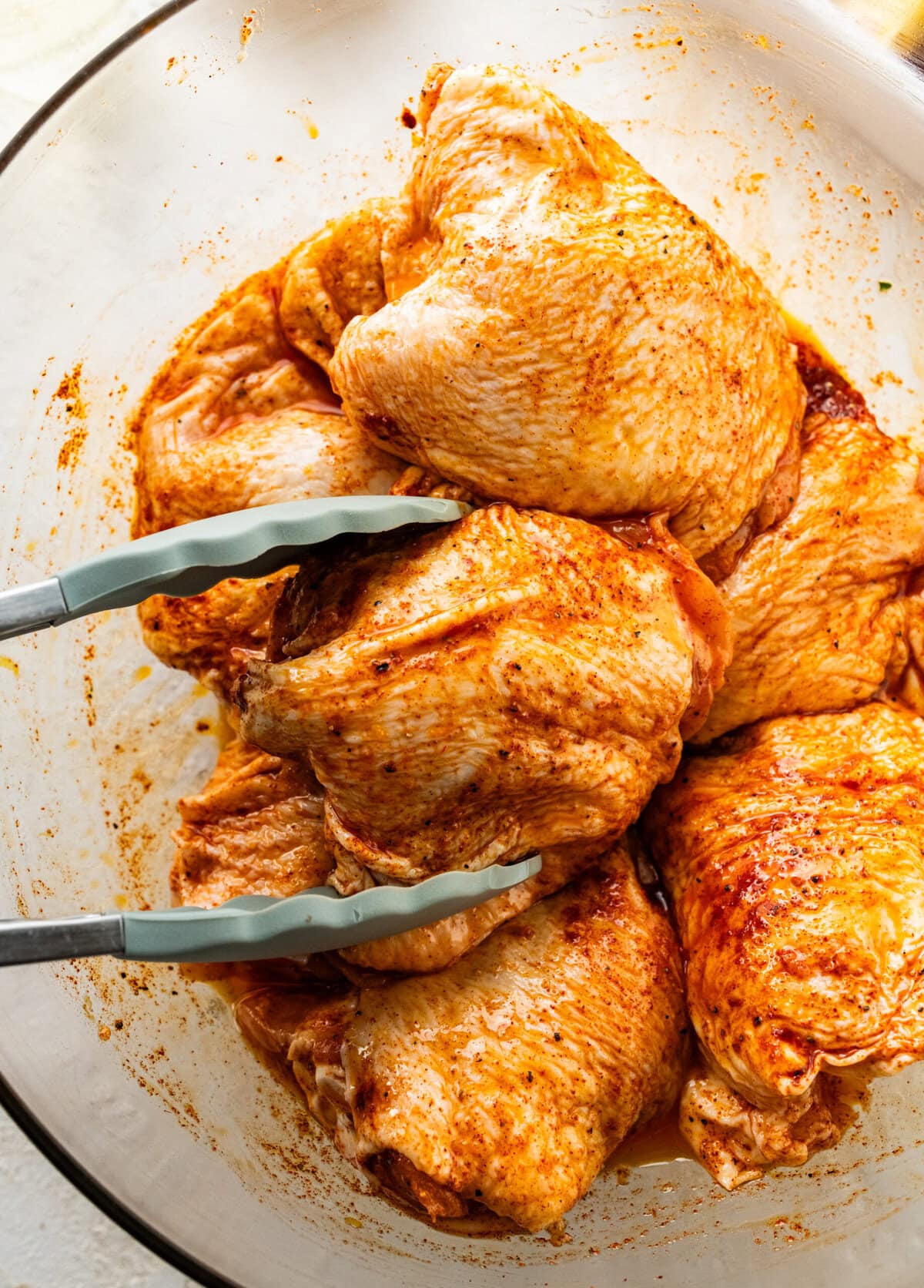 seasoned chicken thighs in a large bowl with tongs grabbing one.