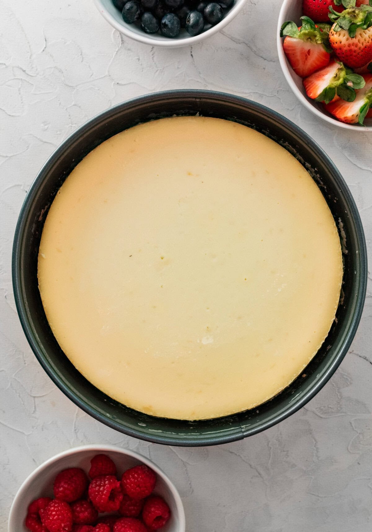 ricotta cheesecake in a springform pan after baked with bowls of fresh berries on the side.
