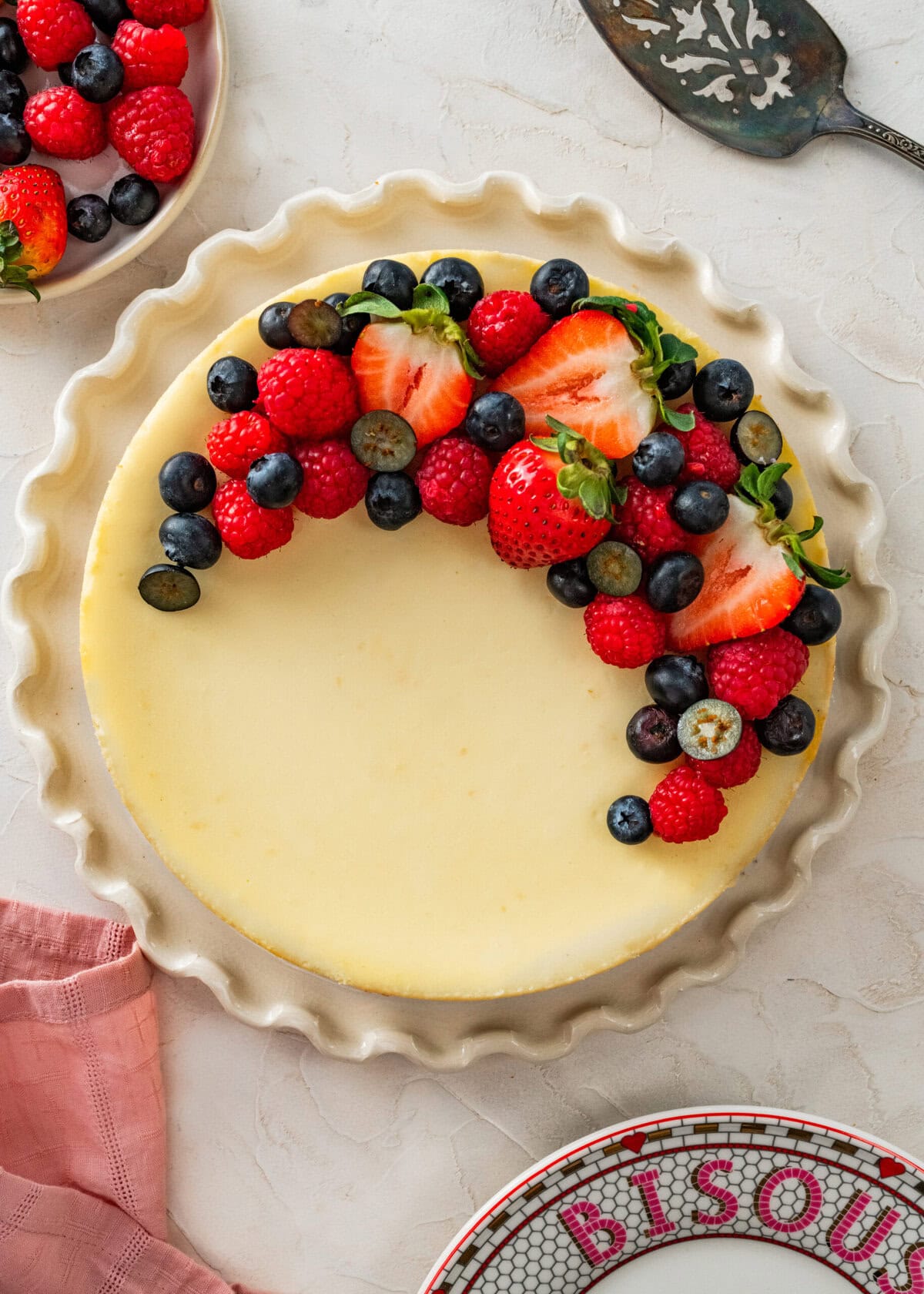 baked ricotta cheesecake topped with fresh berries, with more berries in a bowl on the side.