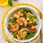 Shrimp asparagus pasta in a bowl, garnished with basil and accompanied by a fork
