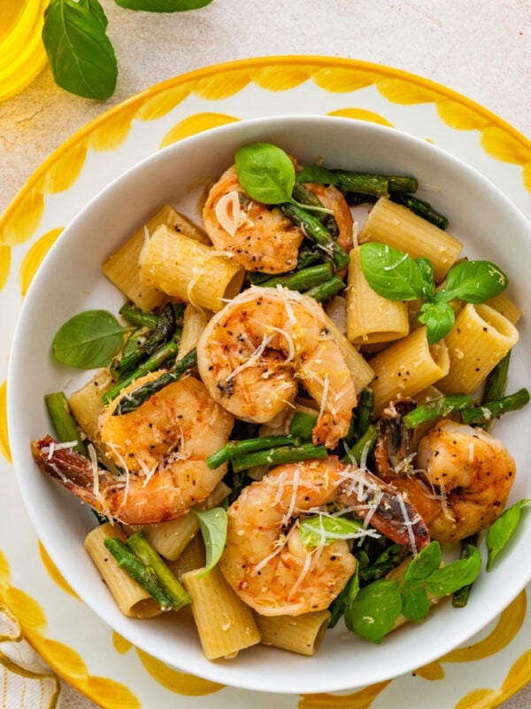 Shrimp asparagus pasta in a bowl, garnished with basil and accompanied by a fork