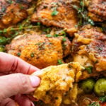 Finger holding up a piece of braised chicken thigh over a plate of the recipe.