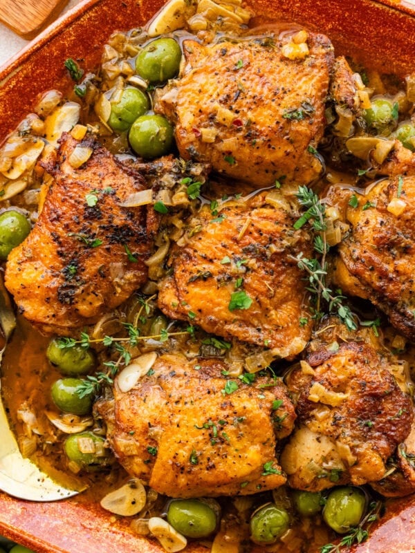 Braised chicken thighs in a bowl topped with garnish and surrounded by other ingredients.