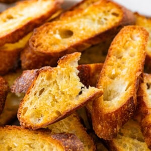 A pile of crostini on a tray with one piece missing a bite.