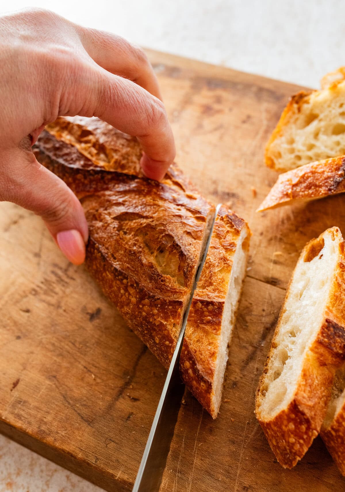 Loaf of bread on a cutting board with a knife cutting slices off and slices laying beside it.