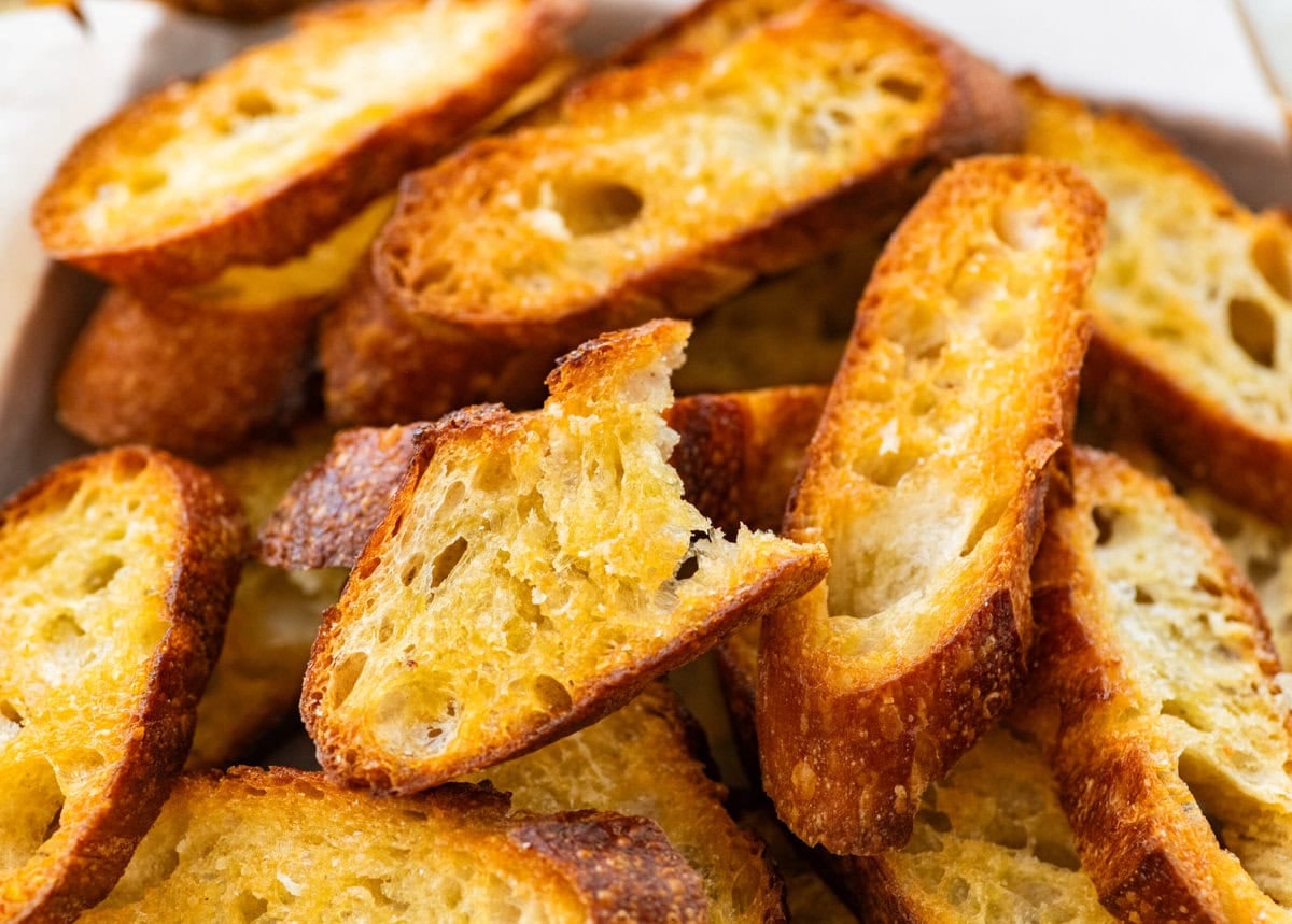 A pile of crostini on a tray with one piece missing a bite.