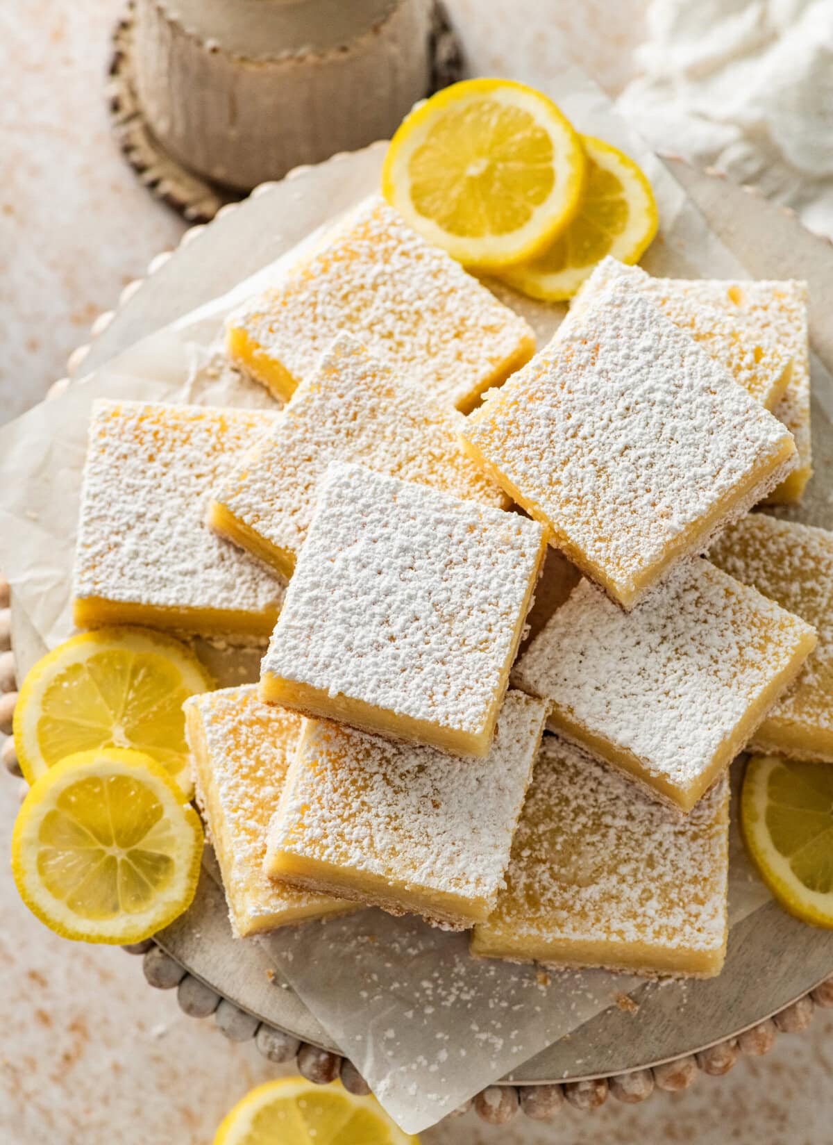 Lemon cream cheese bars topped with powdered sugar displayed on a plate with lemons placed nearby.