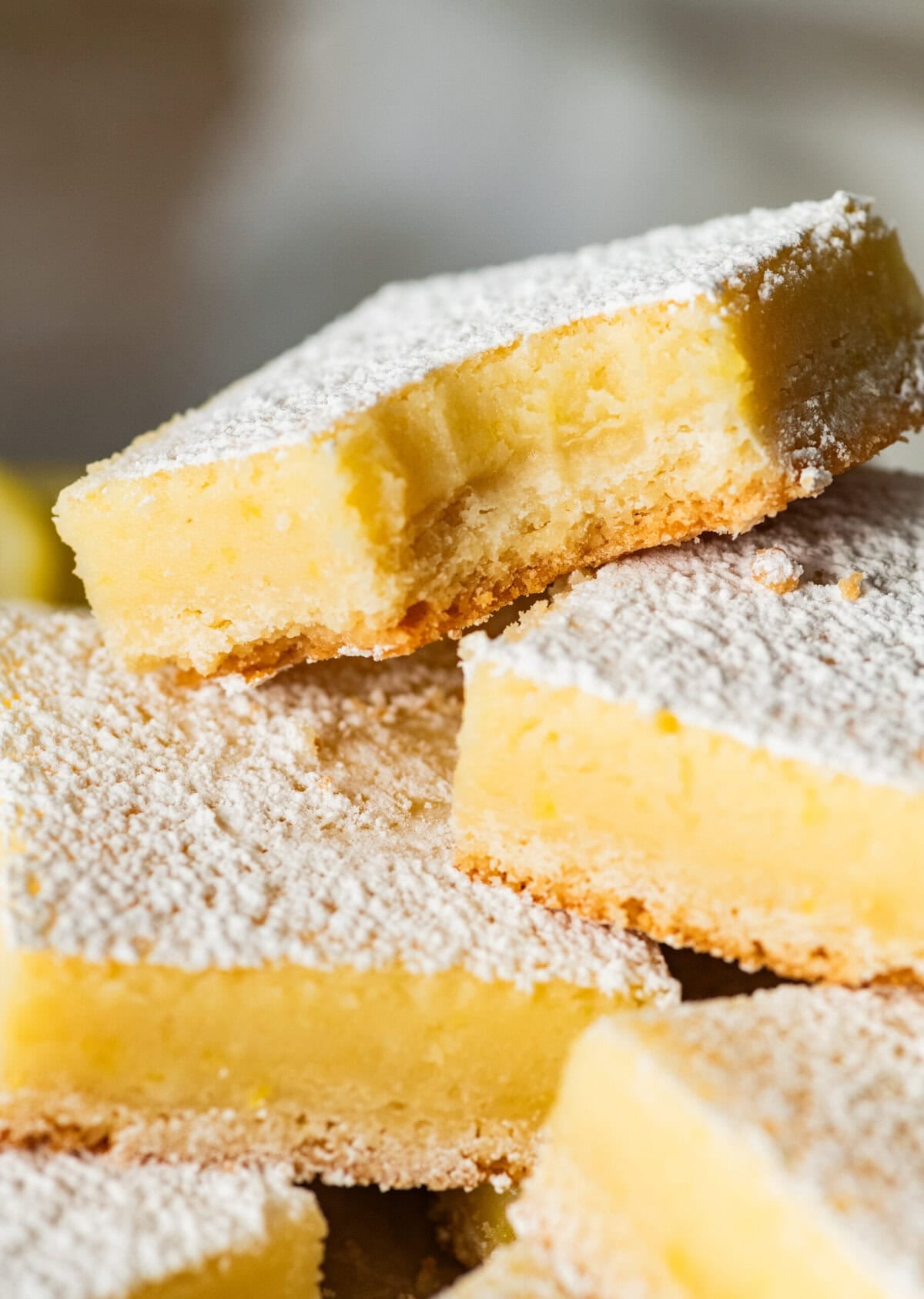 Lemon cream cheese bar with a bite taken out, laying on top of more bars.