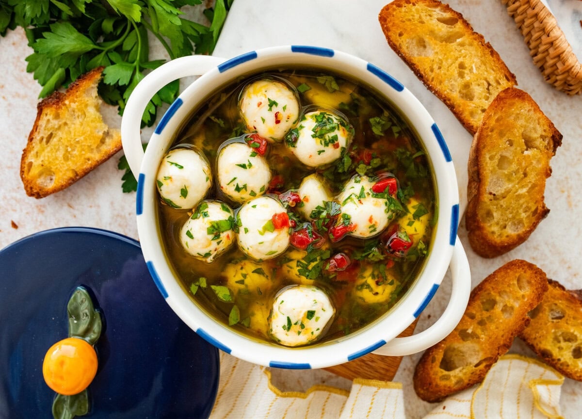 Marinated mozzarella balls in a bowl with ingredients in background.