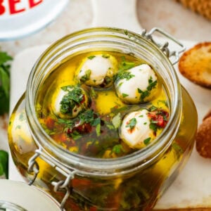 Marinated mozzarella balls in a jar with ingredients in background.