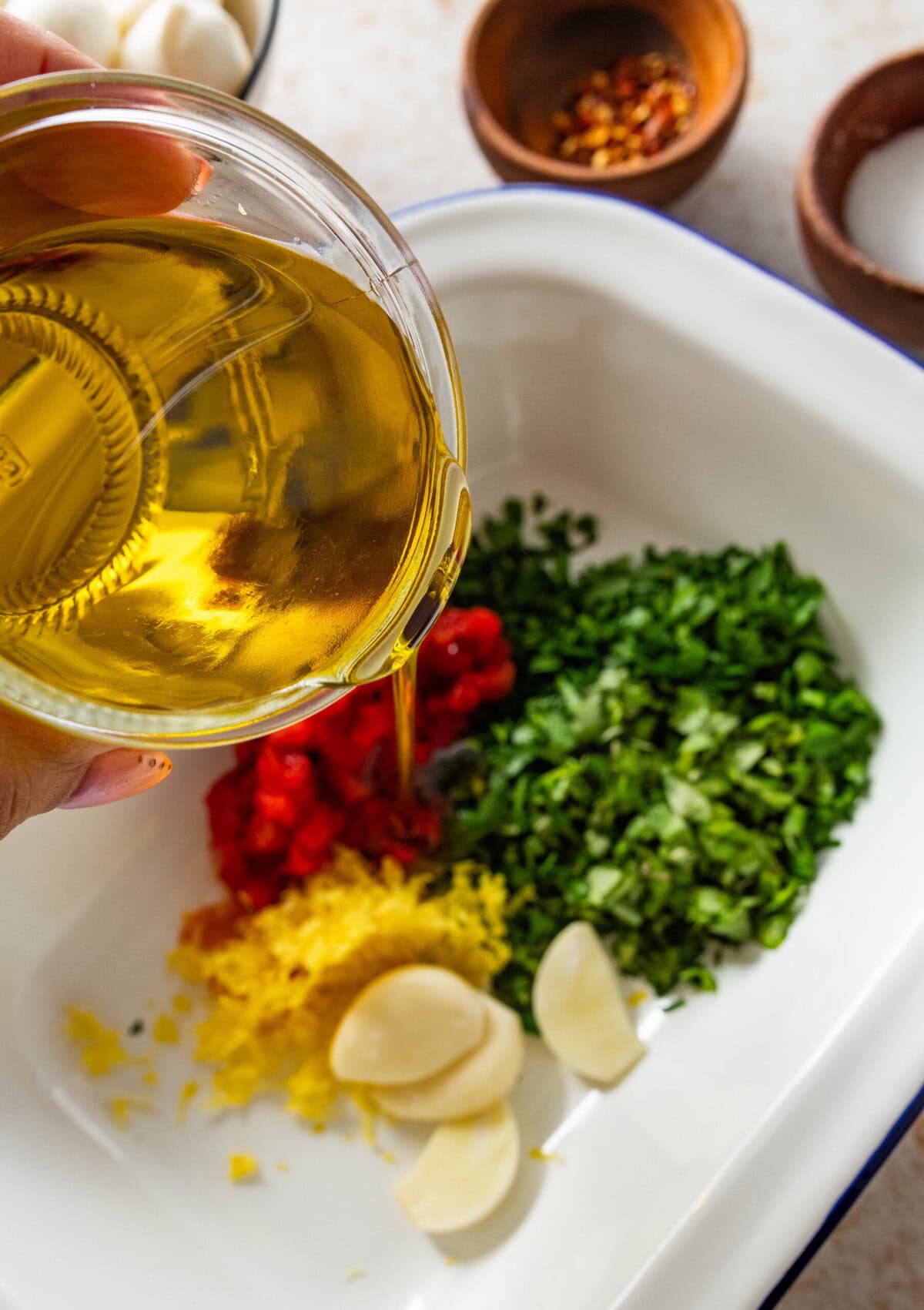 Pouring olive oil from a measuring cup into a dish with the marinade ingredients.