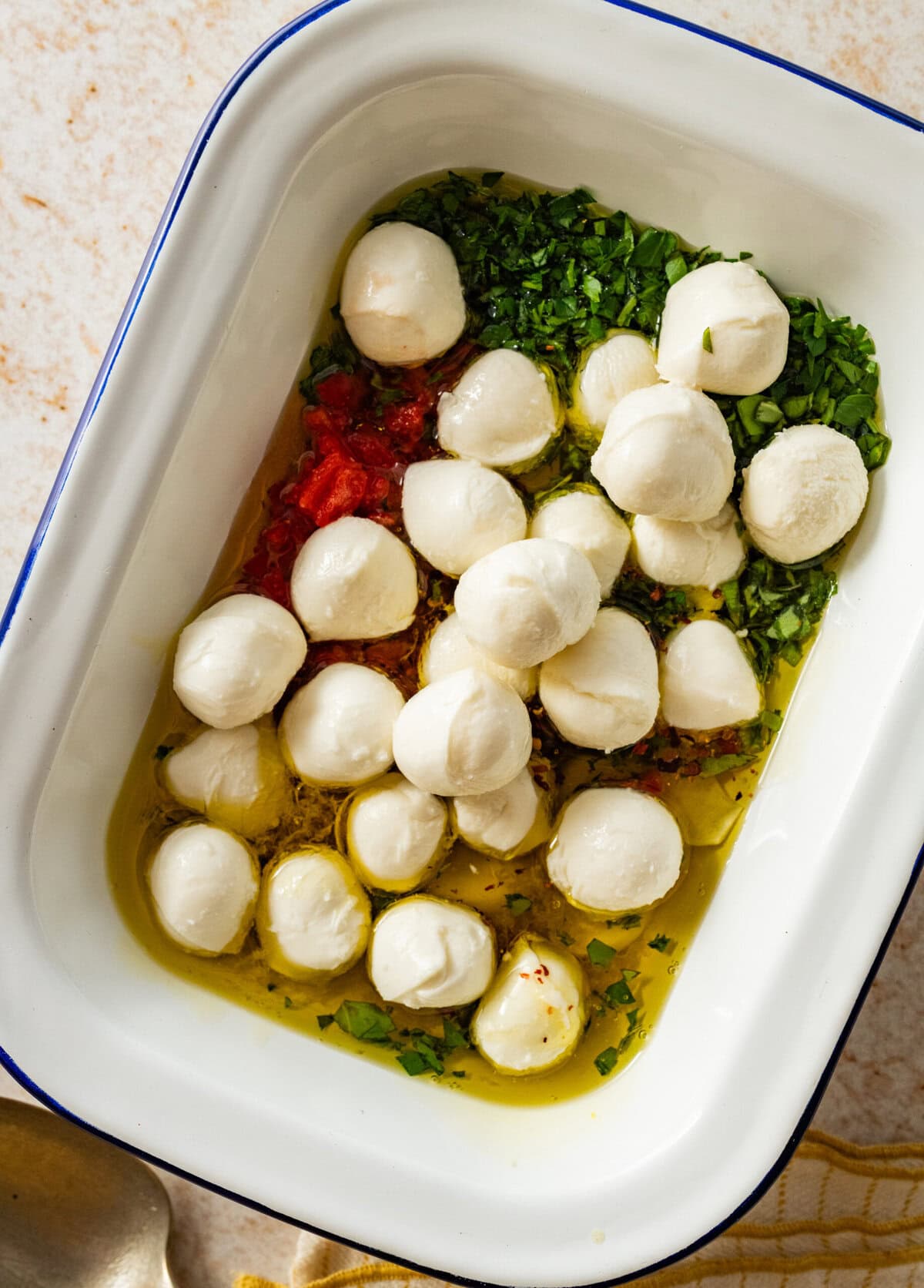Mozzarella balls on top of the marinade ingredients in a dish.