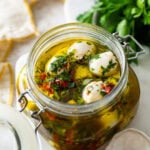 Marinated mozzarella balls in a jar with ingredients in background.