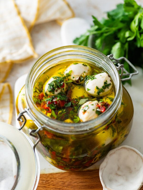 Marinated mozzarella balls in a jar with ingredients in background.