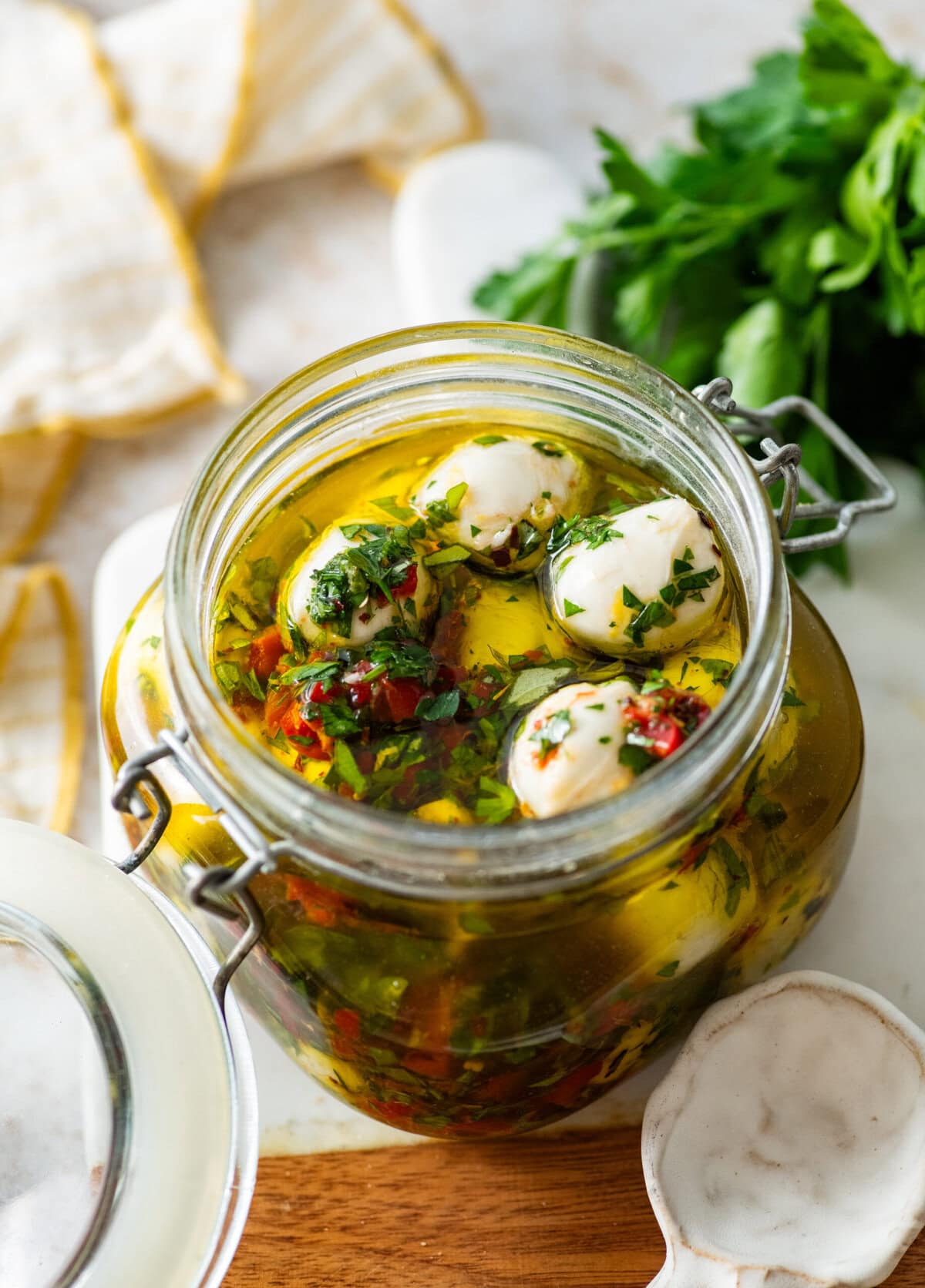 Marinated mozzarella balls in a jar with ingredients in background.