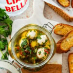 Marinated mozzarella balls in a jar with ingredients in background.