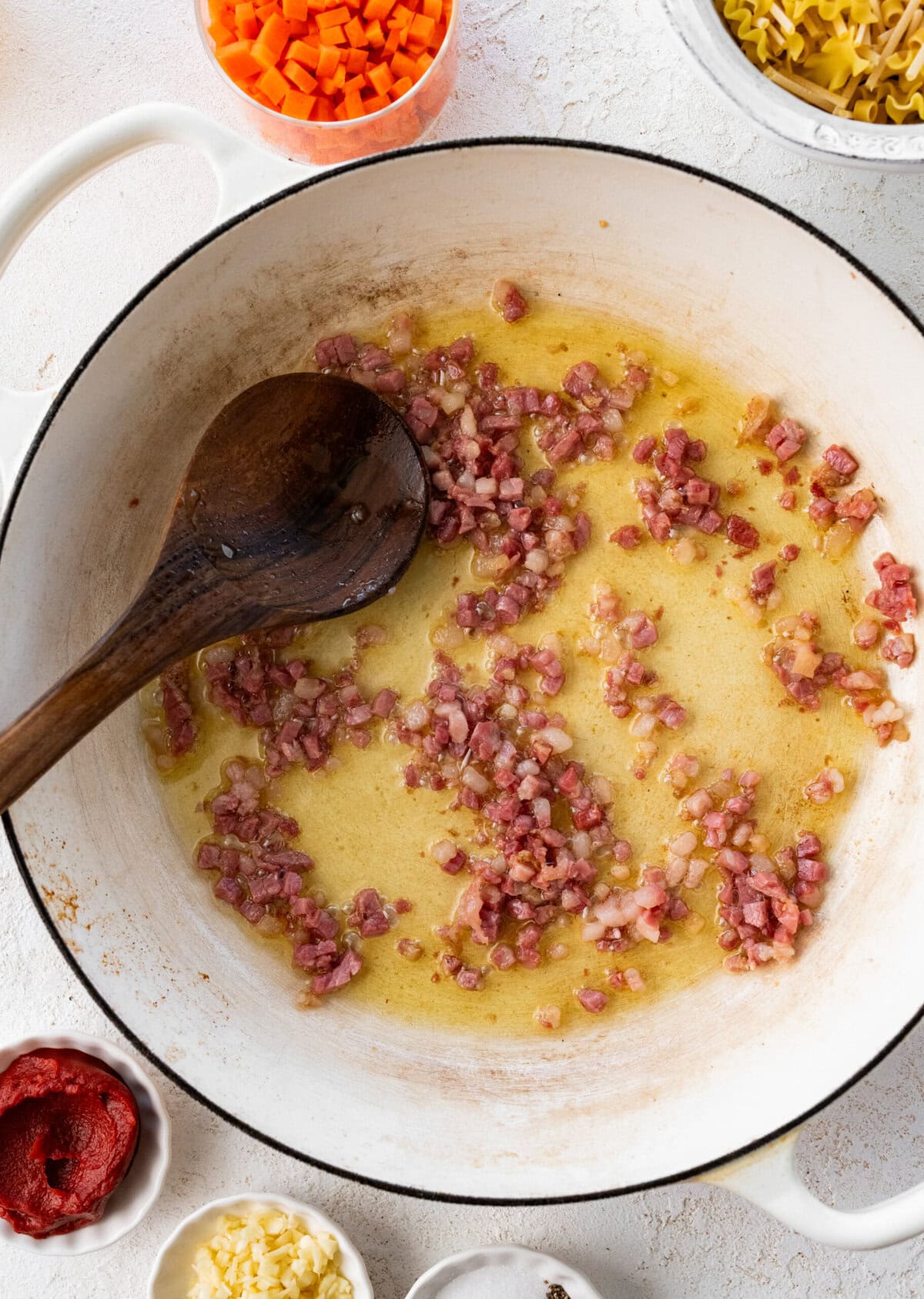 guanciale in a pot with olive oil being stirred with a wooden spoon.