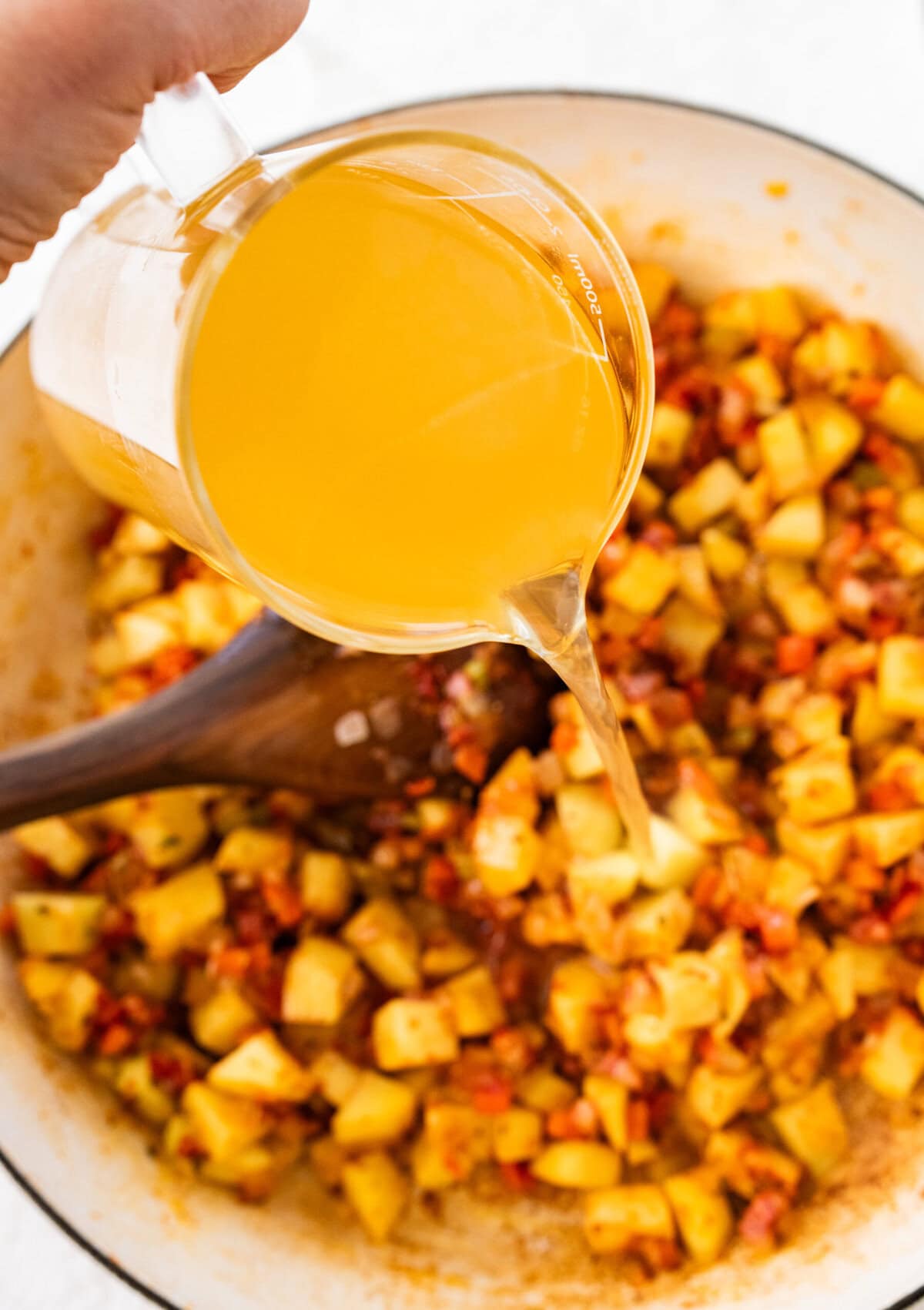 A measuring glass pouring broth over the pot. 