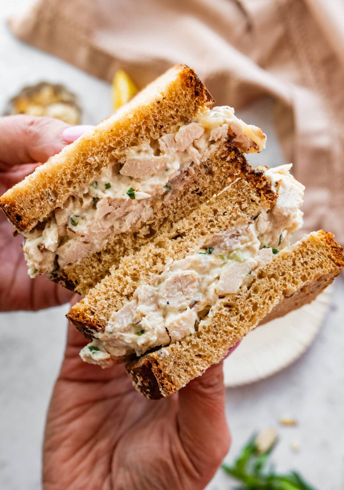 Holding two halves of a tarragon chicken salad sandwich.