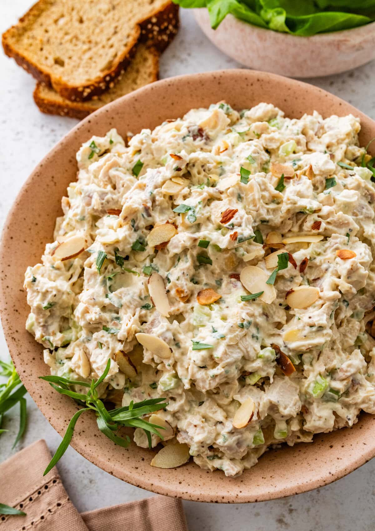 Tarragon chicken salad in a bowl with a serving spoon, with bread and lettuce in the background.