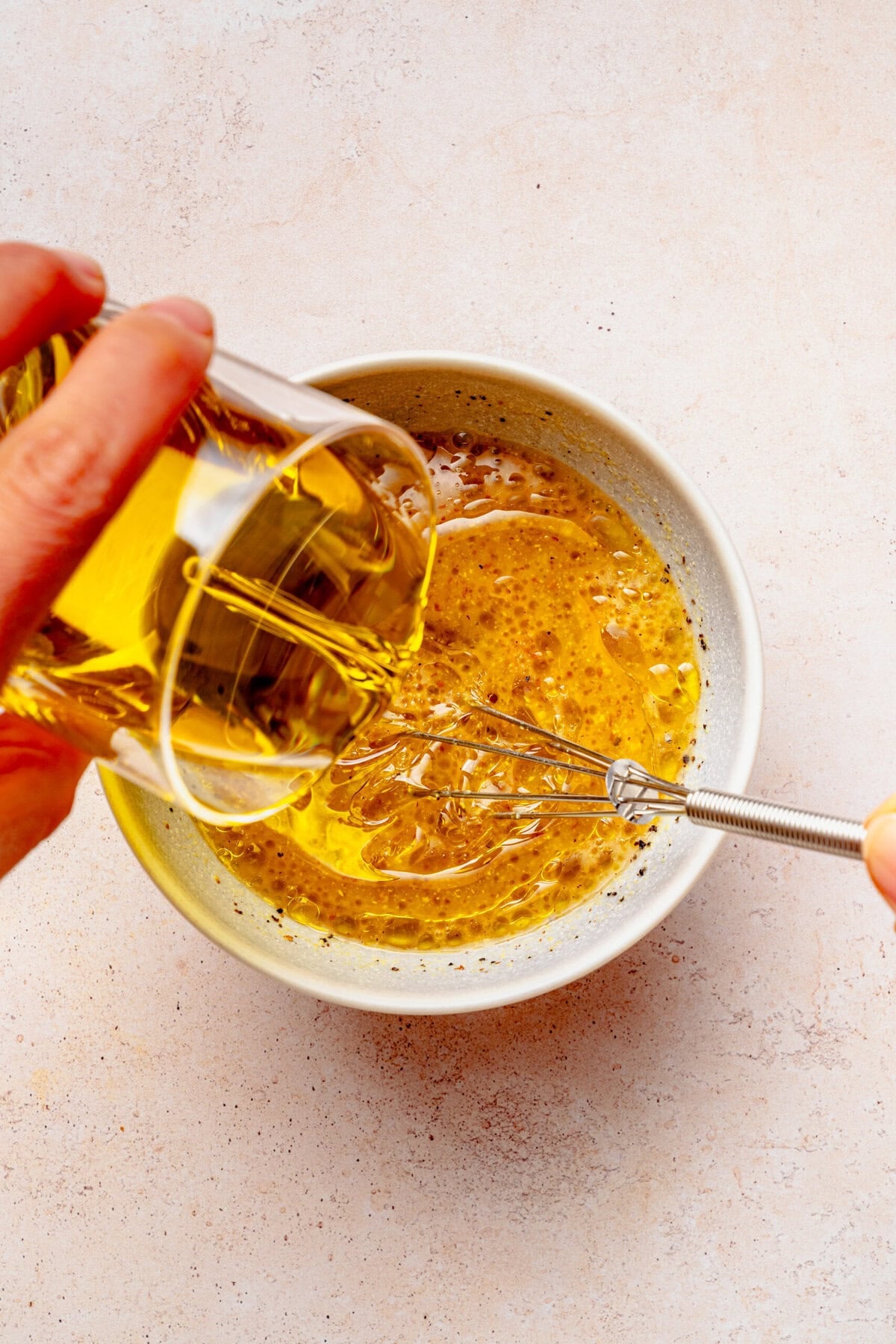 Pouring olive oil into the jar while whisking. 