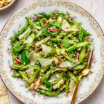 Asparagus salad on a dish with a fork and breadcrumbs nearby in a bowl.