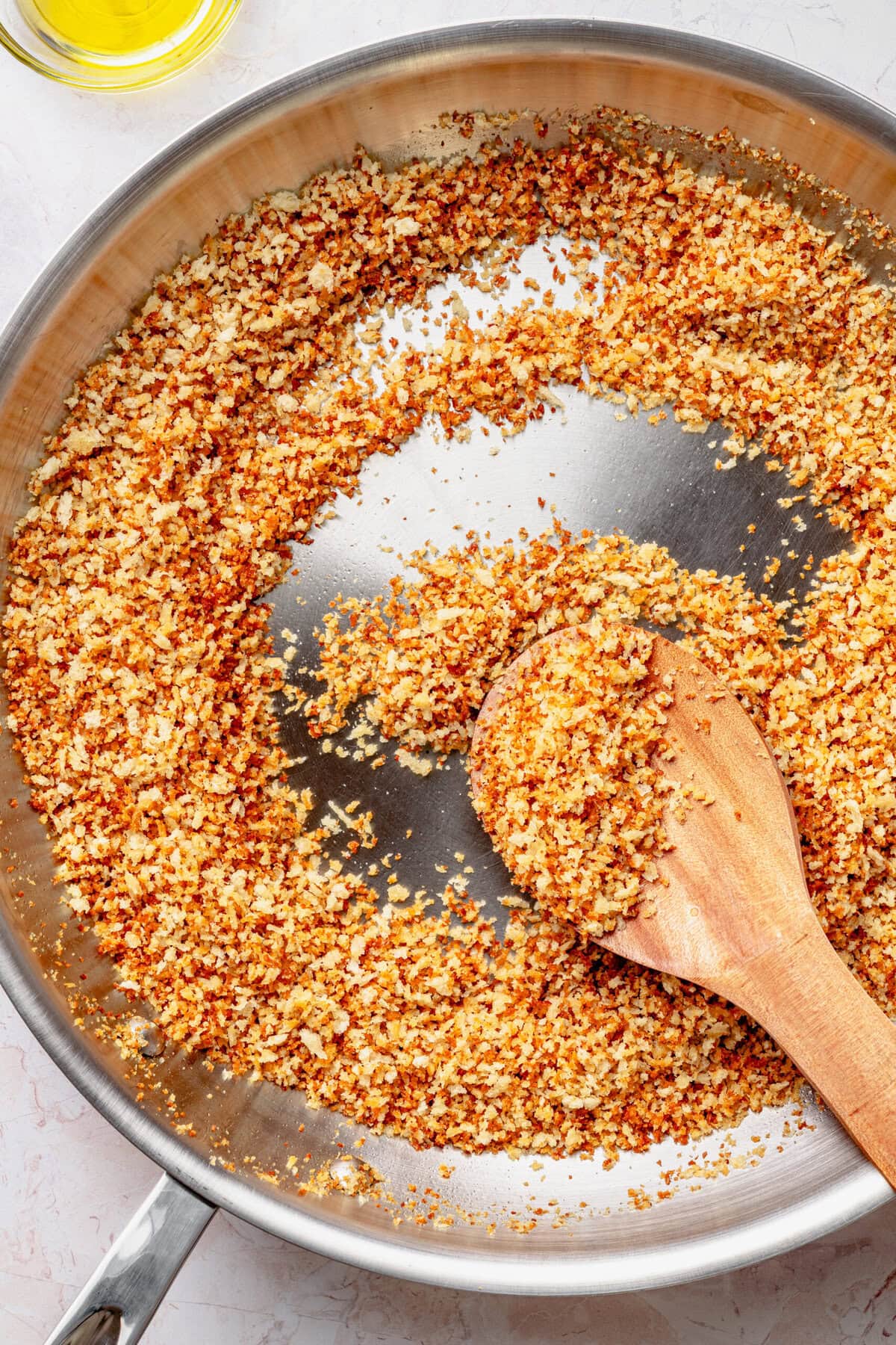 Toasted breadcrumbs in a pan with a wooden spoon stirring,