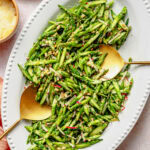 Asparagus salad on a serving dish with serving utensils and extra breadcrumbs in a bowl nearby.