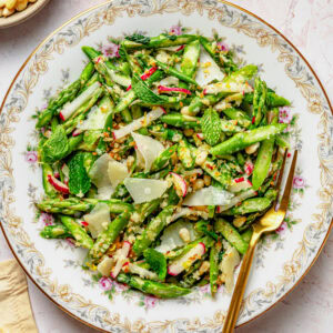 Asparagus salad on a dish with a fork and breadcrumbs nearby in a bowl.