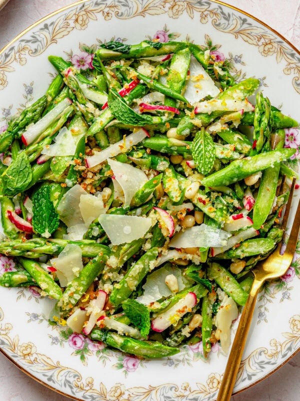 Asparagus salad on a dish with a fork and breadcrumbs nearby in a bowl.
