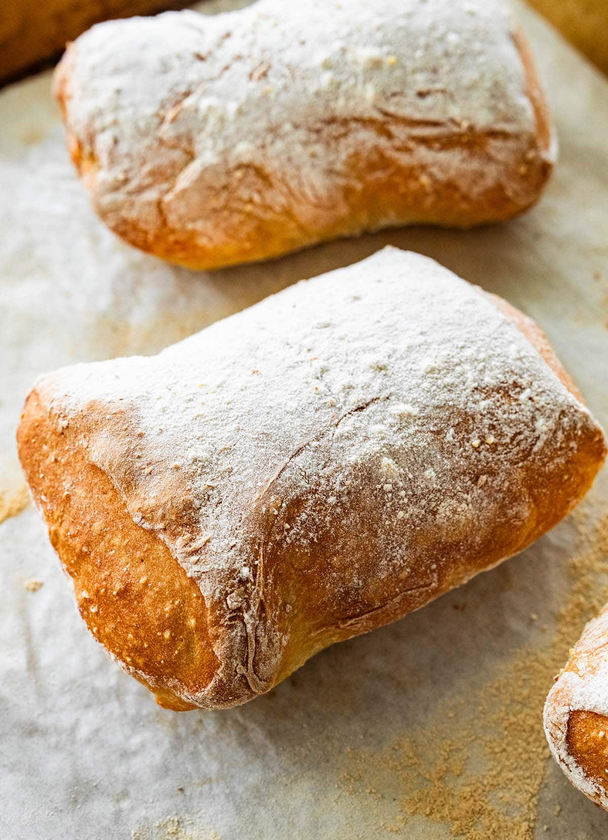 three baked ciabatta loaves on a flour-dusted parchment.