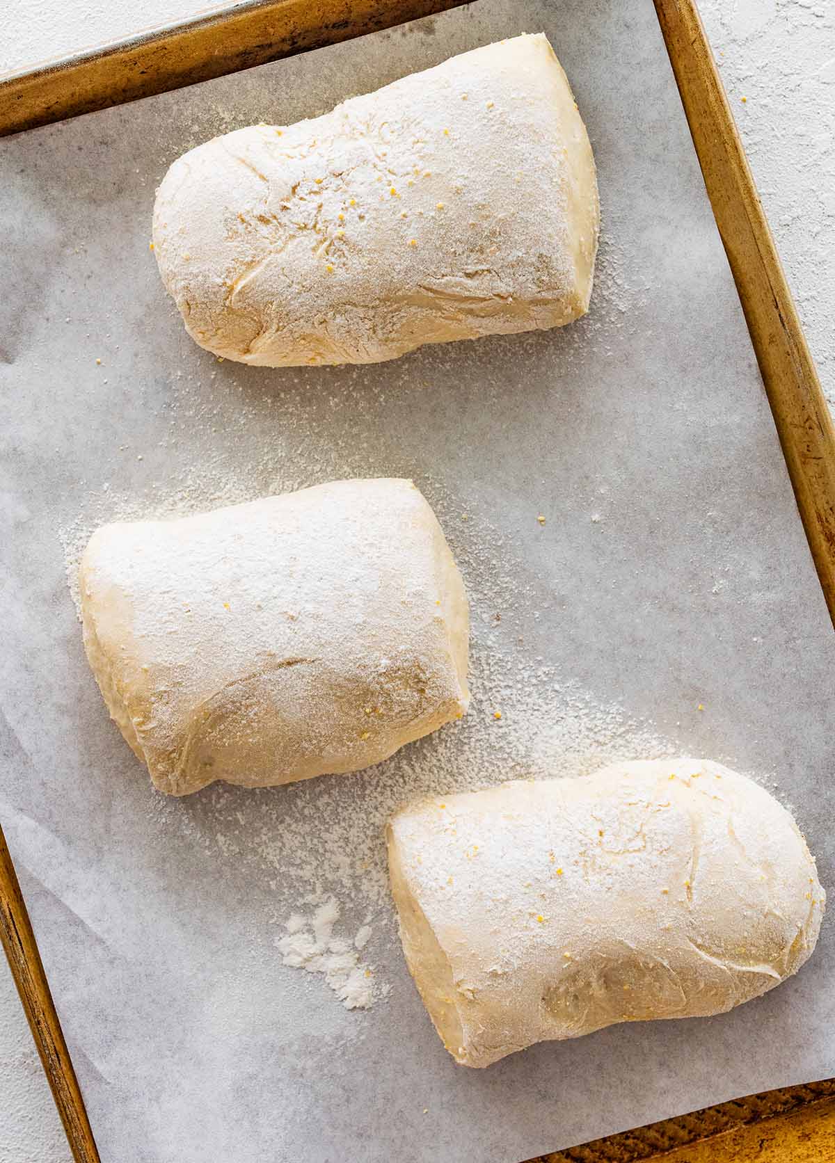 risen ciabatta loaves in a baking tray lined with parchment.
