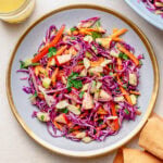 Red cabbage slaw on a plate with another plate nearby, and extra ingredients.