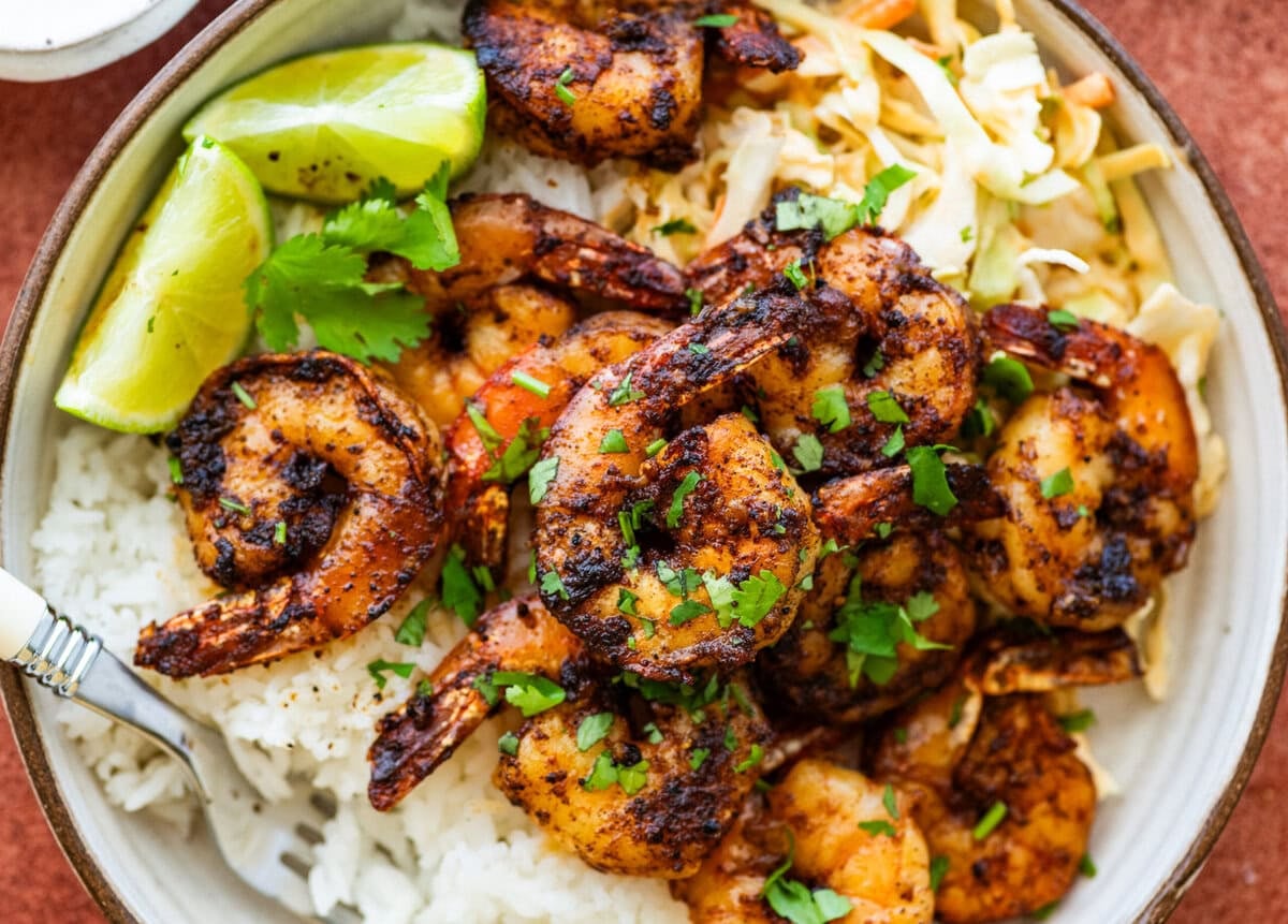 Blackened shrimp on a plate that contains rice and garnish.