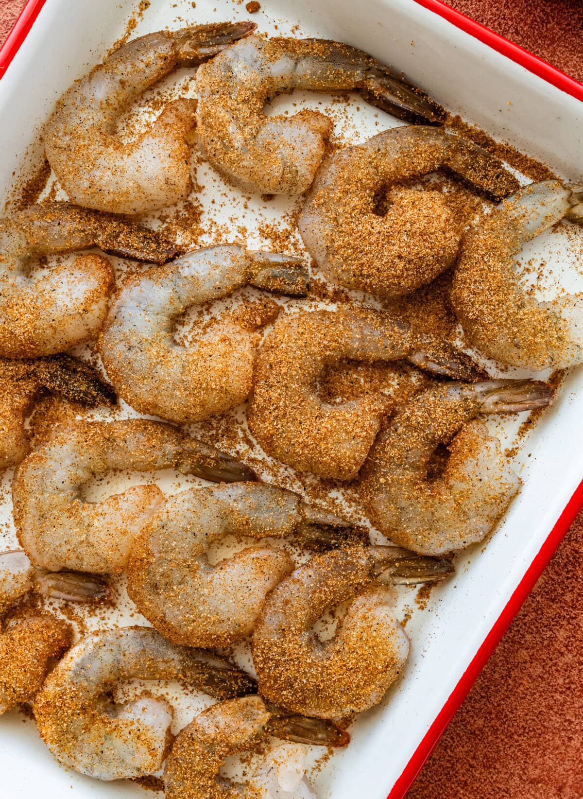 Raw shrimp in a dish covered with blackened seasoning.