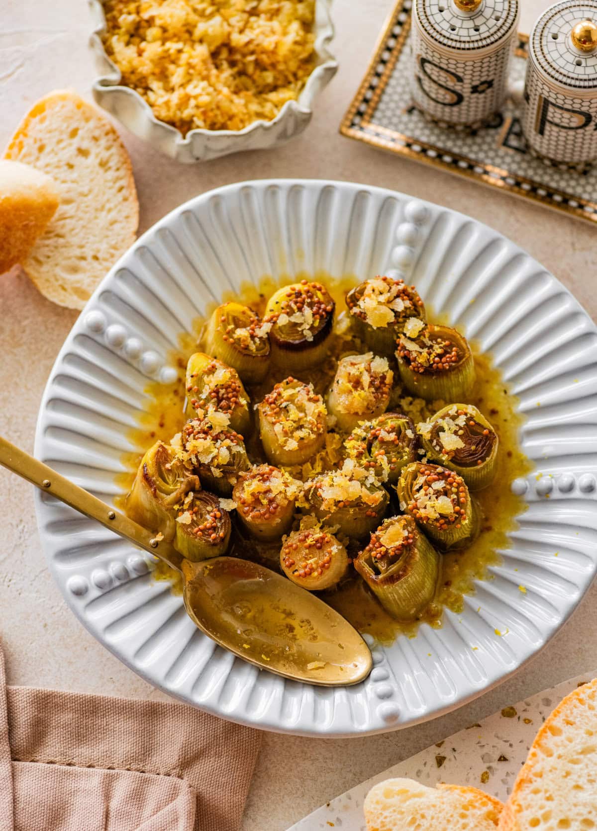 Braised leeks on a serving dish accompanied by a spoon, with more recipe ingredients in the background.
